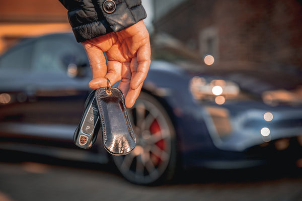 Close-up of bespoke leather tracker holders for Porsche and Vodafone fobs, handcrafted in vegetable-tanned leather with optional initial stamping