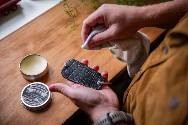 Coupland Leather tracker holder being conditioned with natural leather balm, showing rich vegetable-tanned leather, soft cloth application, and visible patina.