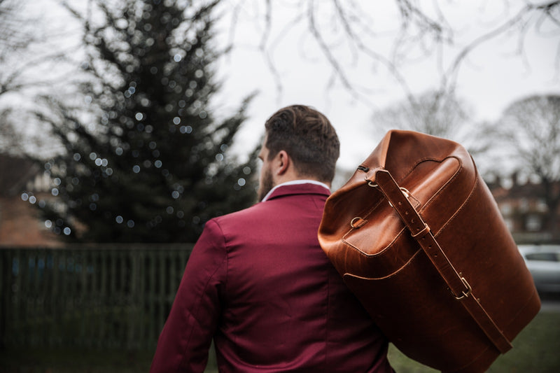 man carrying leather duffle bag on shoulder