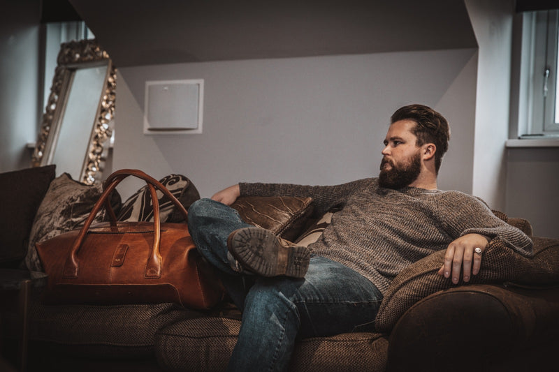 male sitting next to leather duffle bag