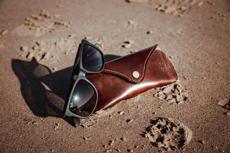 leather sunglasses case on sand with sunglasses